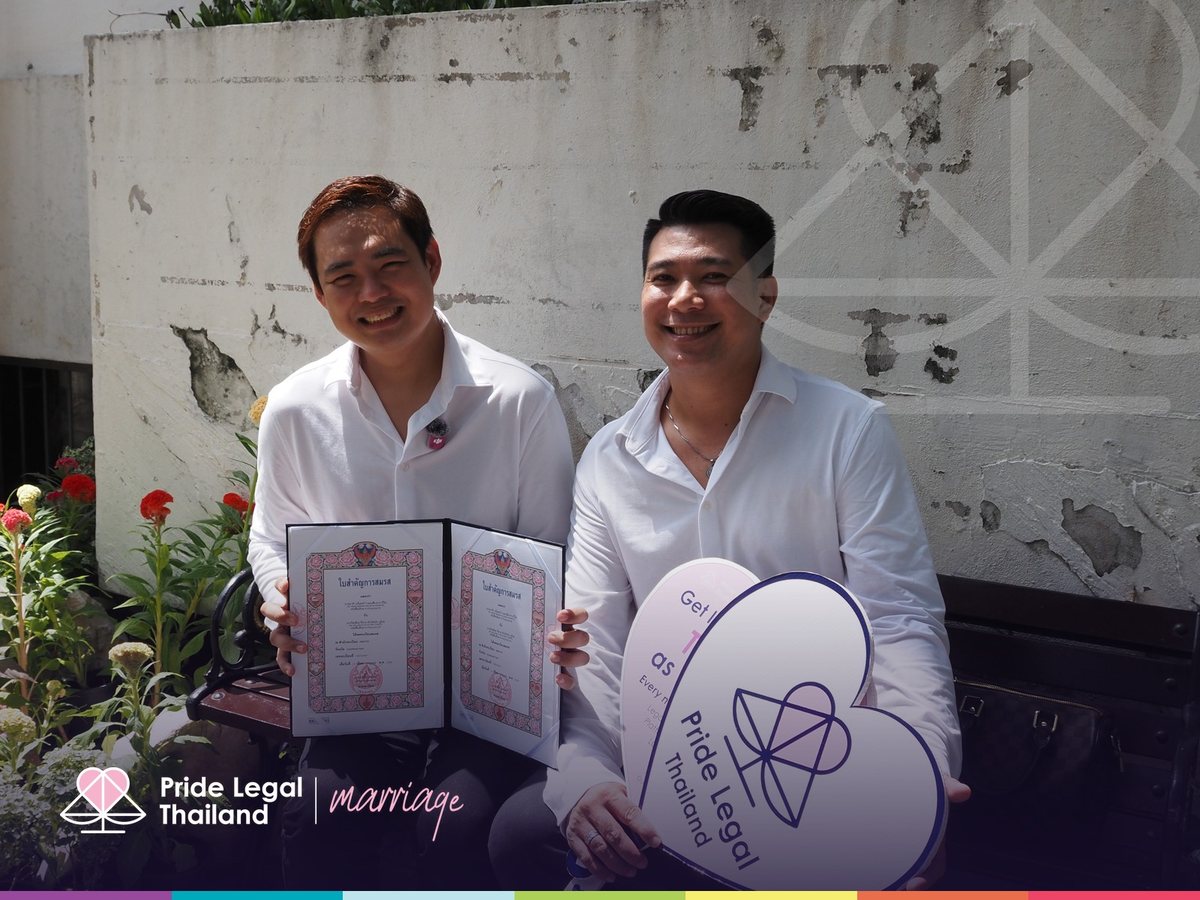Two men in white shirts holding their Thai marriage certificates