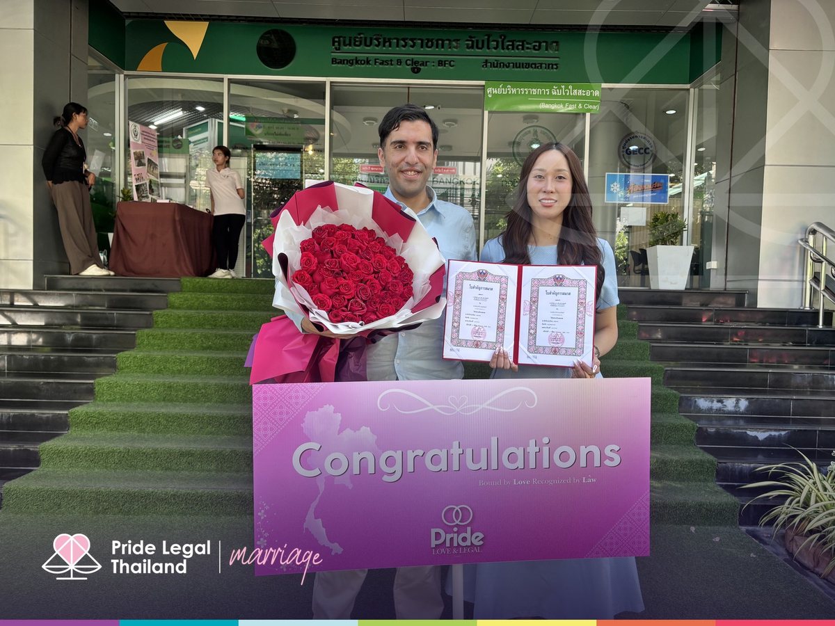 A couple with their marriage certificates and a congratulations sign on the district office steps