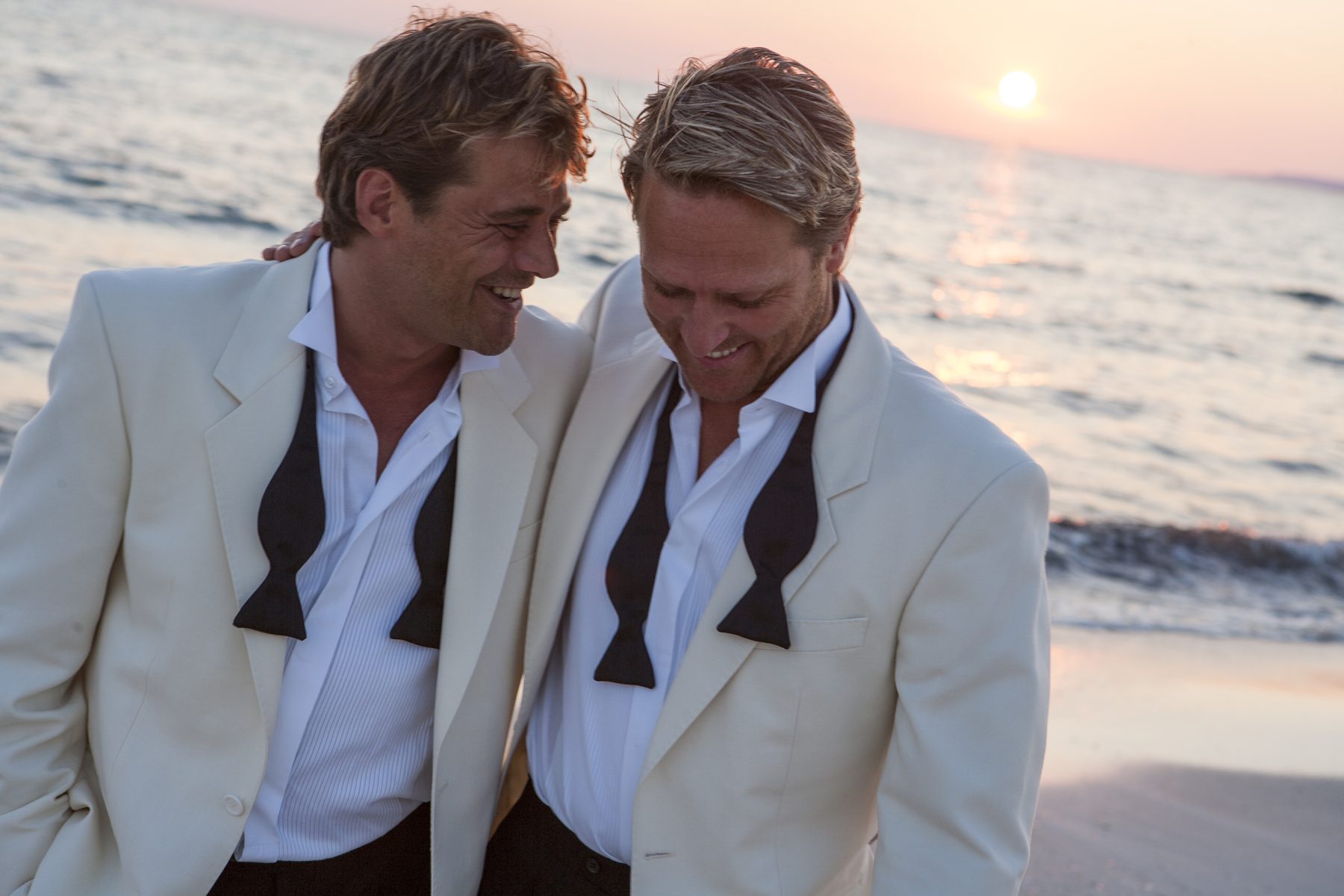 Two grooms laughing on a beach at sunset