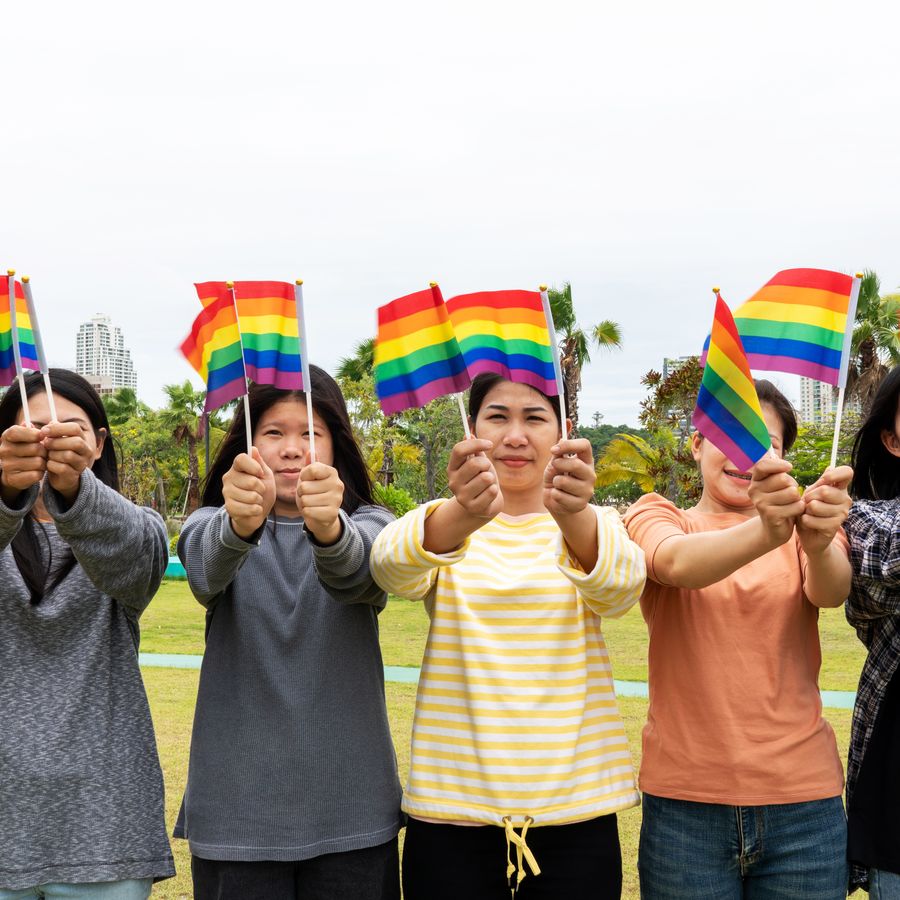 Smiling women holding Pride flags in a city park